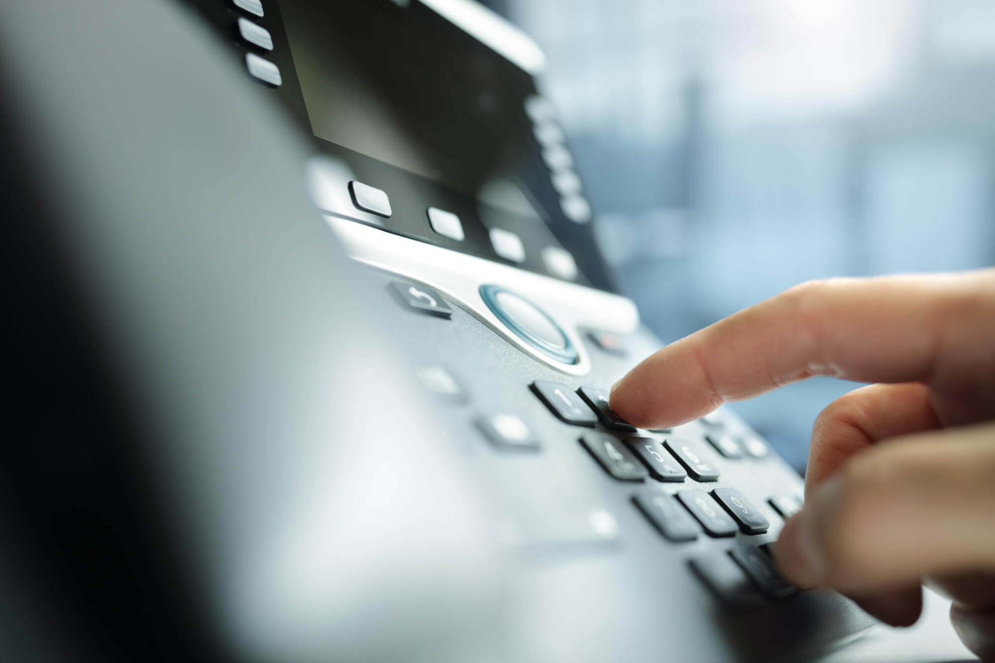 Close up of a hand dialing the touchpad on a desktop IP phone